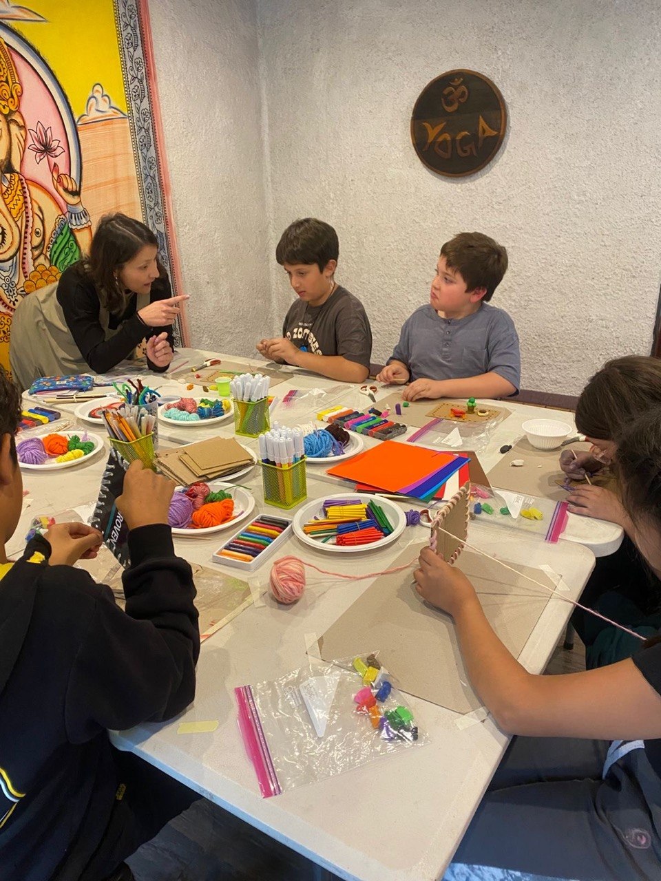Niños tejiendo en telar de cartón junto a una tallerista