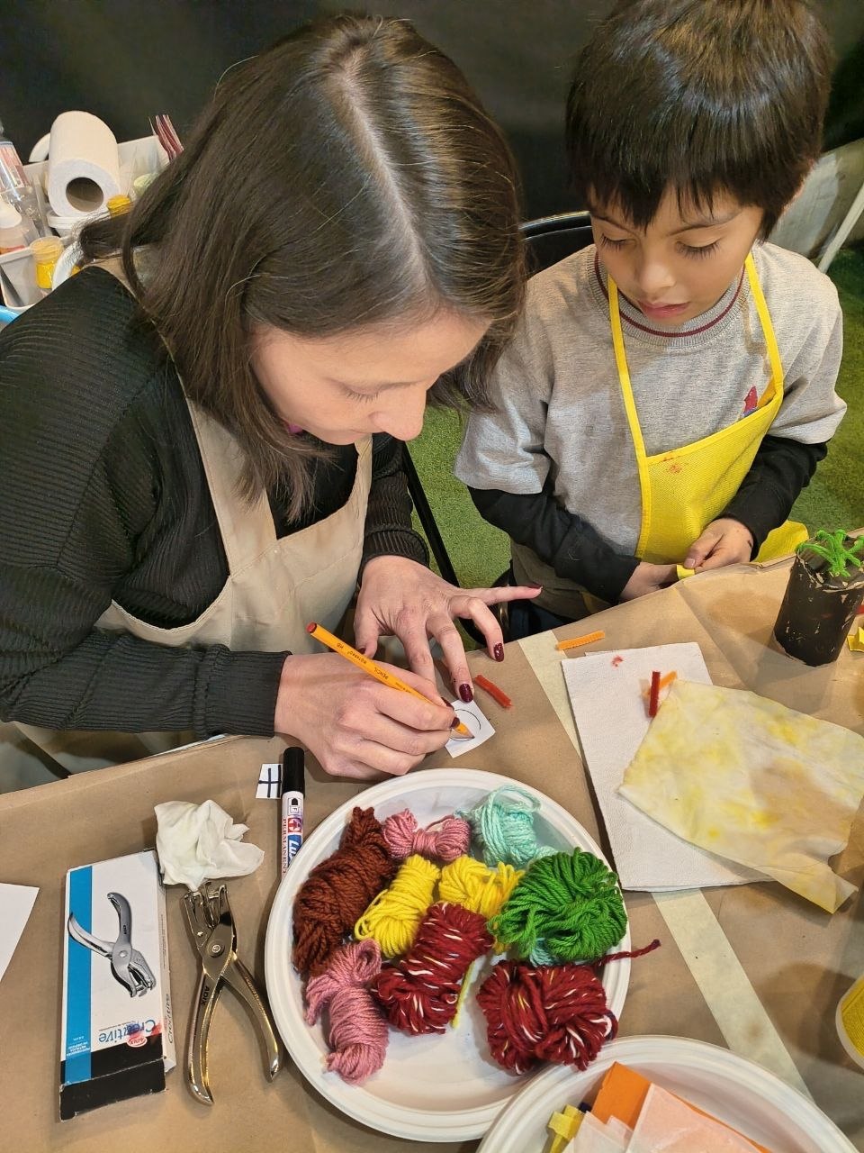 Tallerista guiando a un niño con delantal amarillo en su dibujo